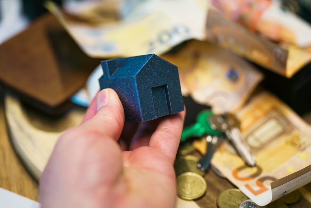 Person’s hand holding a small toy house, money, and keys